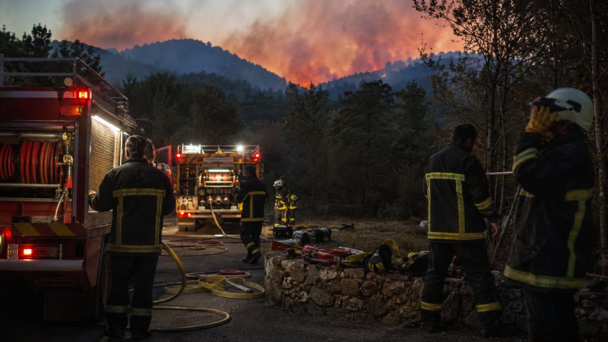 Firefighters preparing equipment near emergency vehicles facing a forest fire.