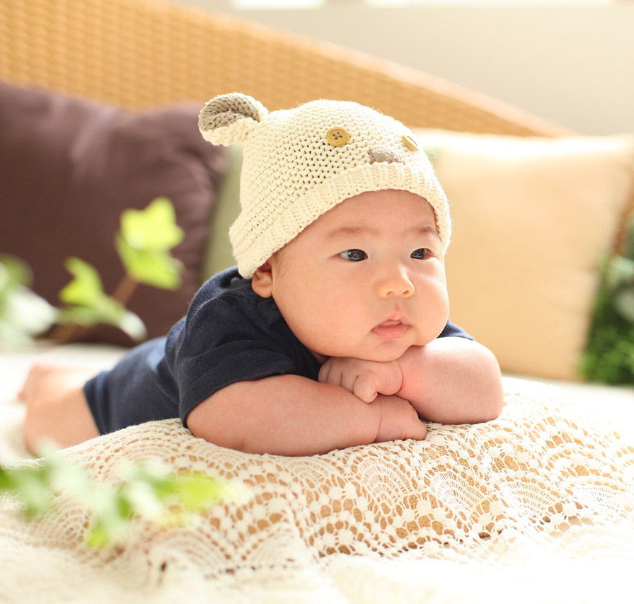 Bebe de 3 meses tumbado en una alfombra de juego sonriendo y alcanzando juguetes coloridos