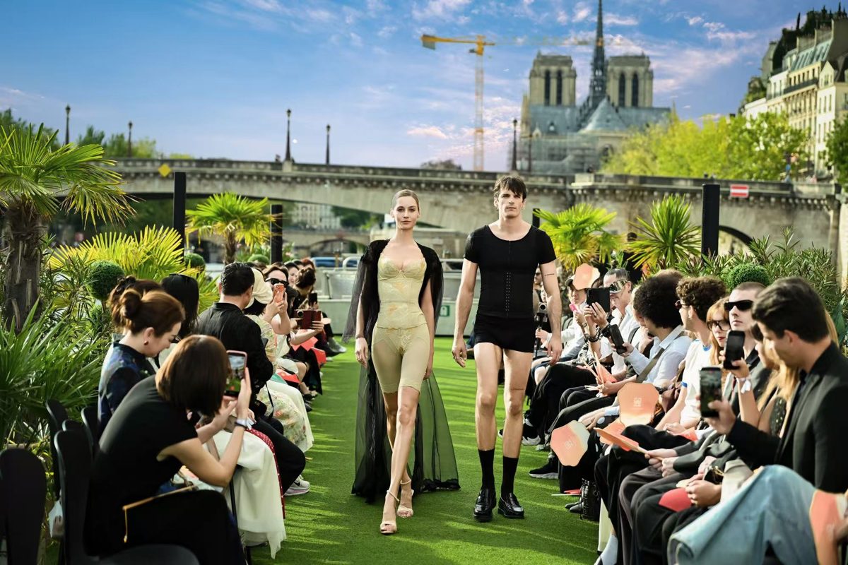 Modelle che sfilano in lingerie modellante YuMei East sul ponte di un battello, davanti a Notre-Dame de Paris e al pubblico